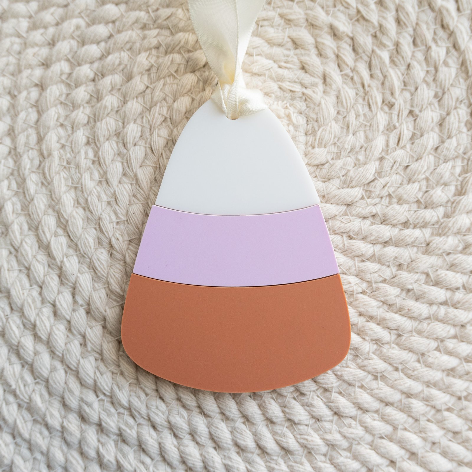An acrylic bag tag of a candy in the shape of corn with orange, lavender and white stripes