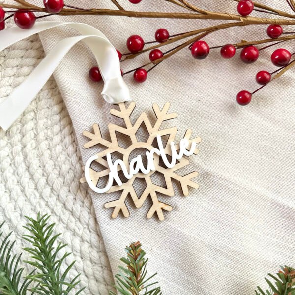 A wooden Christmas ornament in the shape of a snowflake with the name Charlie on top in white acrylic