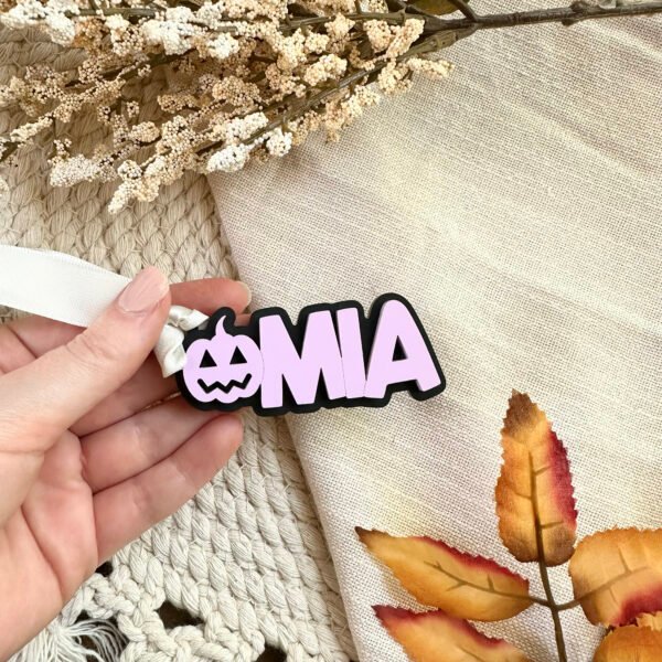 A lavender and black acrylic key chain with a pumpkin followed by the name Mia