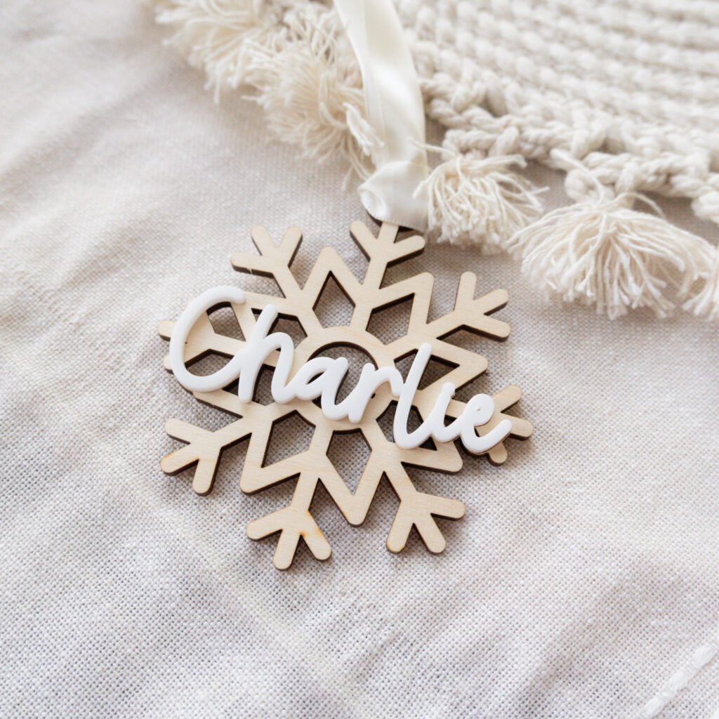 A wooden Christmas ornament in the shape of a snowflake with the name Charlie on top in white acrylic