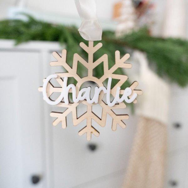 A wooden Christmas ornament in the shape of a snowflake with the name Charlie on top in white acrylic